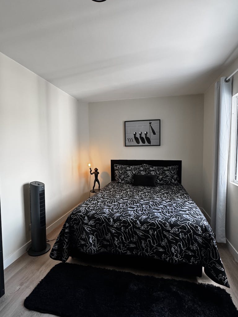 A bright, minimalist bedroom featuring abstract-patterned bedding, a stylish lamp, and modern decor.